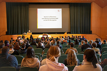 Erstsemester-Studierende sitzen als Publikum in einem Hörsaal während Sie von der Rektorin begrüßt werden. 