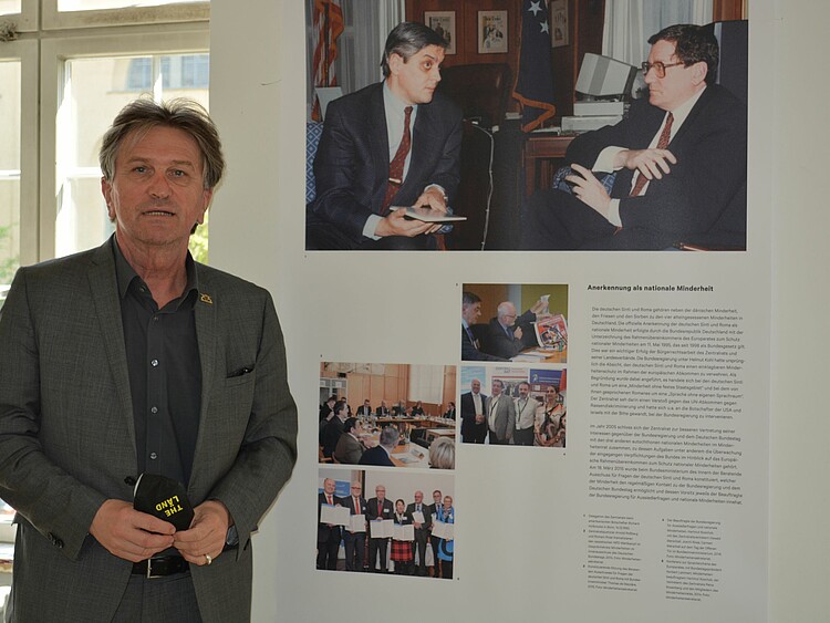 Minister Manfred Lucha steht vor einem Bild der Ausstellung