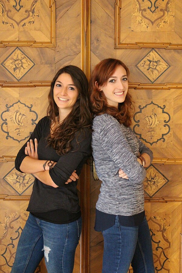 Das Bild zeigt zwei Studentinnen der BA Logopädie. Sie stehen mit überkreuzten Armen Schulter an Schulter vor einer braunen Tür.