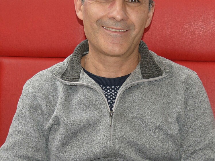 Profilbild von Arash Malek, der auf einem roten Sofa sitzt